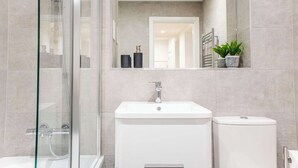 Et moderne badeværelse med en brusekabine i glas, en hvid vask og et toilet.