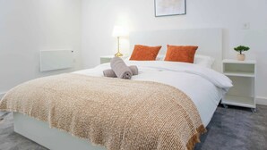 En pænt redt seng med et beige dynebetræk, to orange puder, en hvid sengegavl og en senget lampe.