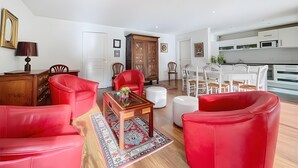 Uma sala de estar moderna com sofás de couro vermelho, uma mesa de centro de madeira e uma área de refeições com cadeiras brancas.