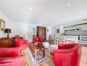 A modern living room with red leather sofas, a wooden coffee table, and a dining area with white chairs. - Central Antibes 4-Person Apartment with Terrace, Garden & Parking – Riva Park (Antibes)