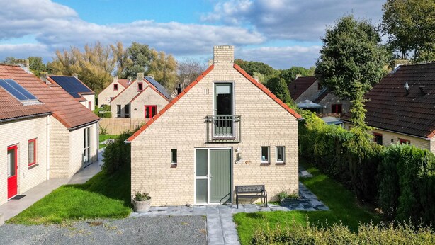 Ett litet hus byggt av tegel med en röd dörr, en balkong och en grusuppfart.