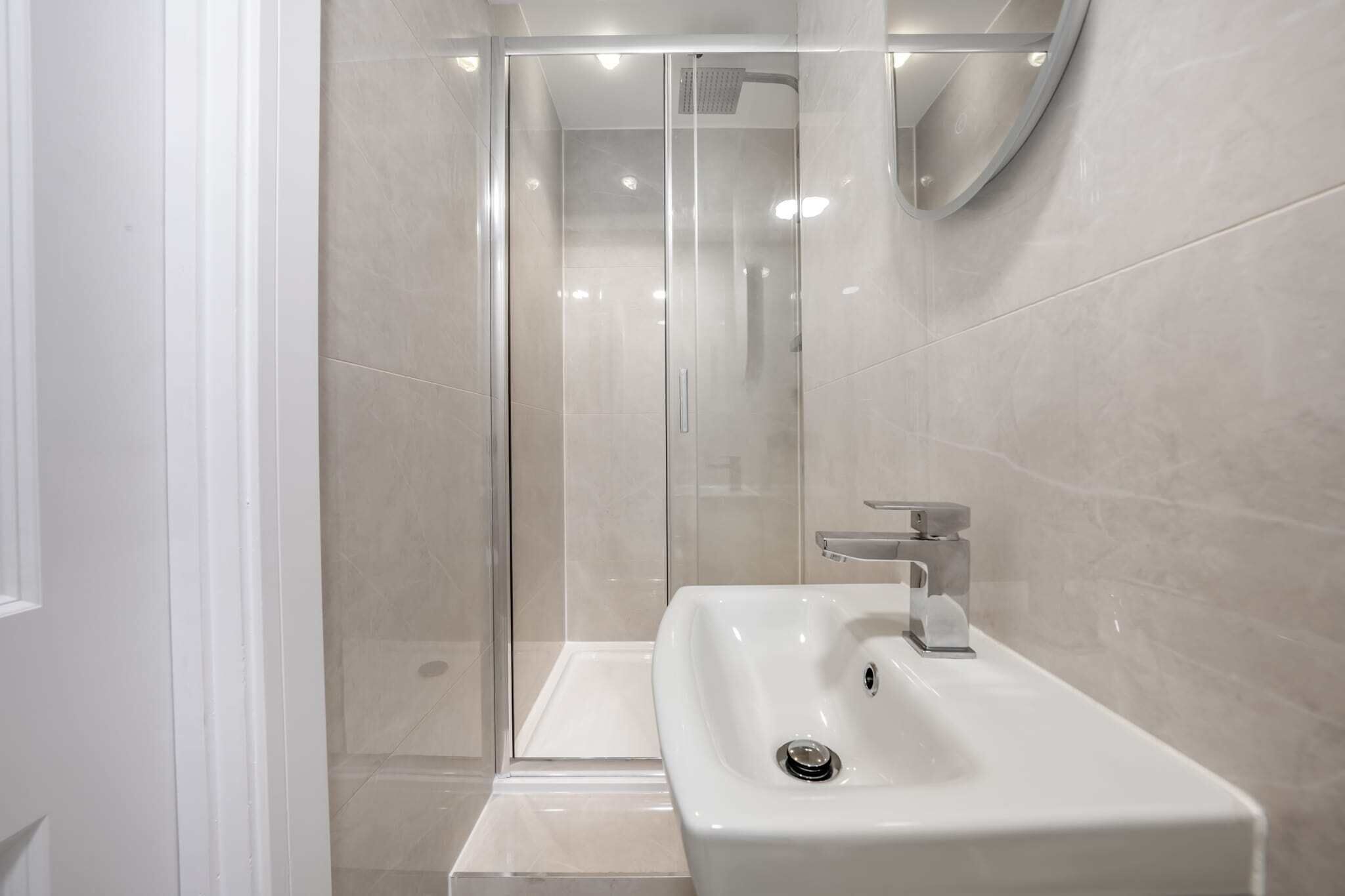 Uma casa de banho moderna com chuveiro em cabine de vidro, lavatório branco e espelho.