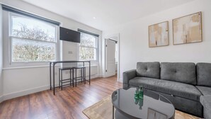 En moderne stue med en grå sofa, et rundt sofabord og et fjernsyn monteret på væggen.