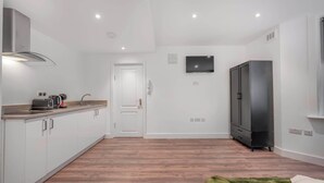 A modern kitchen with white cabinets, a stainless steel range hood, a flat-screen TV, and a black refrigerator. - Standard Studio in Knightsbridge (London)