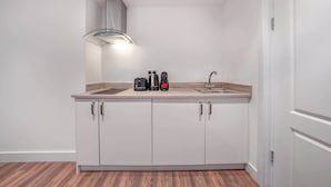 A modern kitchen with white cabinets, a stainless steel range hood, a double sink, and a countertop with a coffee maker and kettle. - Standard Studio in Knightsbridge (London)