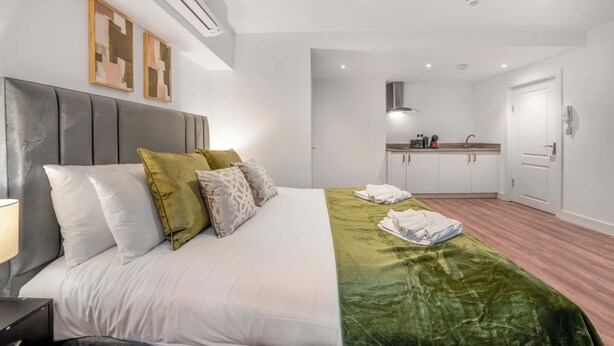 A hotel room with a bed, a bedside table, a nightstand, a green bedspread, a white wall, a white ceiling, a white door, a white wall-mounted air conditioner, a white ceiling-mounted light fixture, a white wall-mounted telephone, a white wall-mounted light switch, a white wall-mounted smoke detector, a white wall-mounted thermostat, a white wall-mounted clock, a white wall-mounted power outlet, a white wall-mounted light switch, a white wall-mounted light switch, a white wall-mounted light switch, a white wall-mounted light switch, a white wall-mounted light switch, a white wall-mounted light switch, a white wall-mounted light switch, a white wall-mounted light switch, a white wall-mounted light switch, a white wall-mounted light switch, a white wall-mounted light switch, a white wall-mounted light switch, a white wall-mounted light switch, a white wall-mounted light switch, a white wall-mounted light switch, a white wall-mounted light switch, - Standard Studio in Knightsbridge (London)