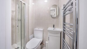Uma casa de banho moderna com chuveiro em cabine de vidro, sanita branca, lavatório com espelho e suporte para toalhas.