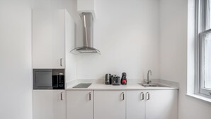 Cozinha moderna com armários brancos, micro-ondas embutido, exaustor de aço inoxidável, pia e janela.