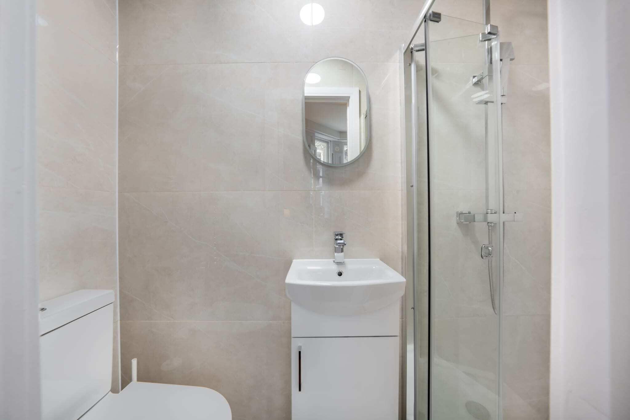 A bathroom with a toilet, a sink, a mirror, and a glass-enclosed shower.