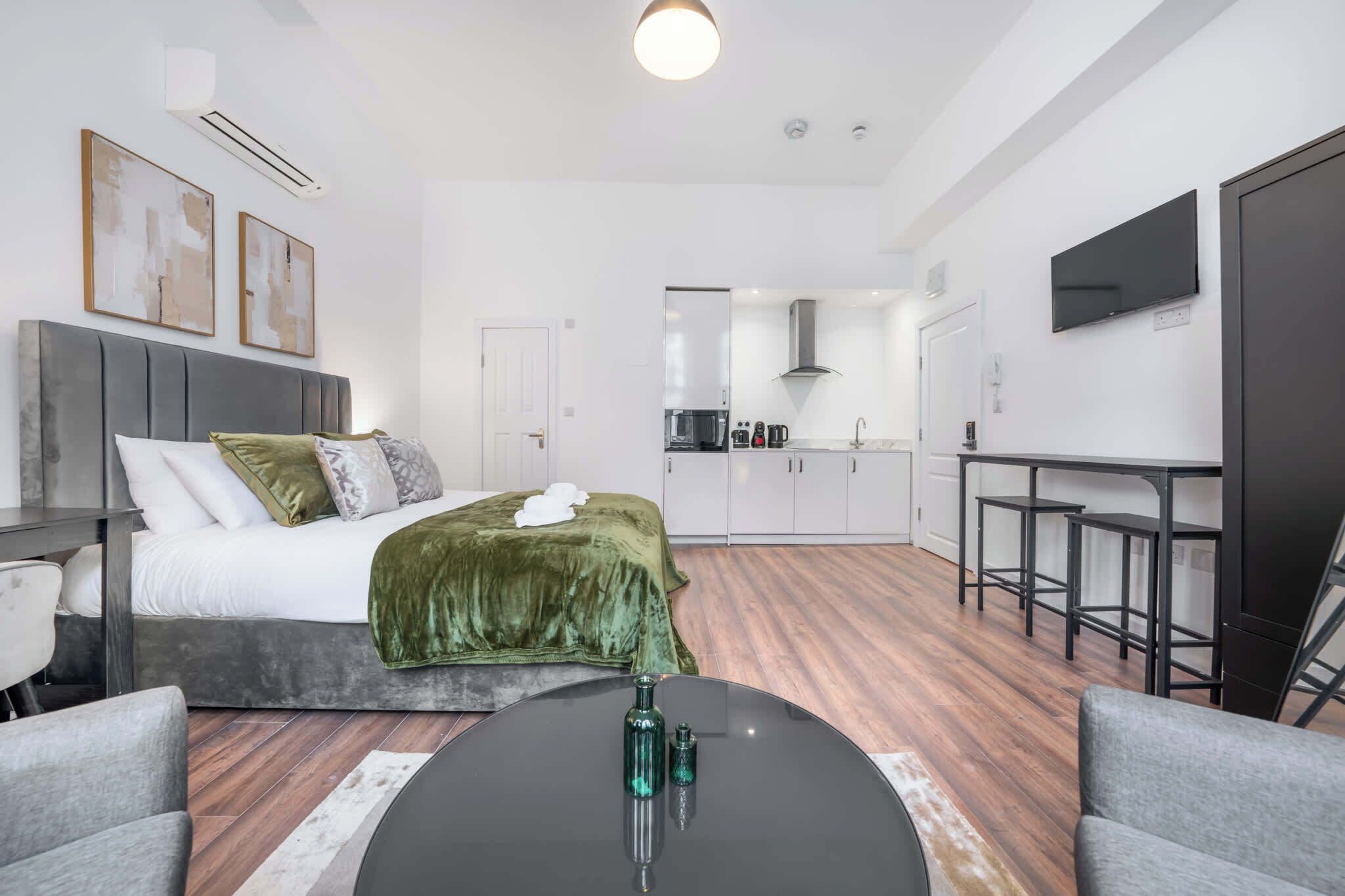 Una habitación de hotel moderna con cama, una mesa de comedor, televisor y espacio de cocina.