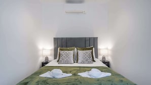 A hotel room with a bed, two bedside lamps, a headboard, and two towels on the bed. - Charming One Bedroom Flat in Knightsbridge (London)