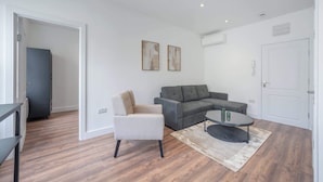 A modern living room with a grey sectional sofa, a beige armchair, a coffee table, and a white door. - Charming One Bedroom Flat in Knightsbridge (London)