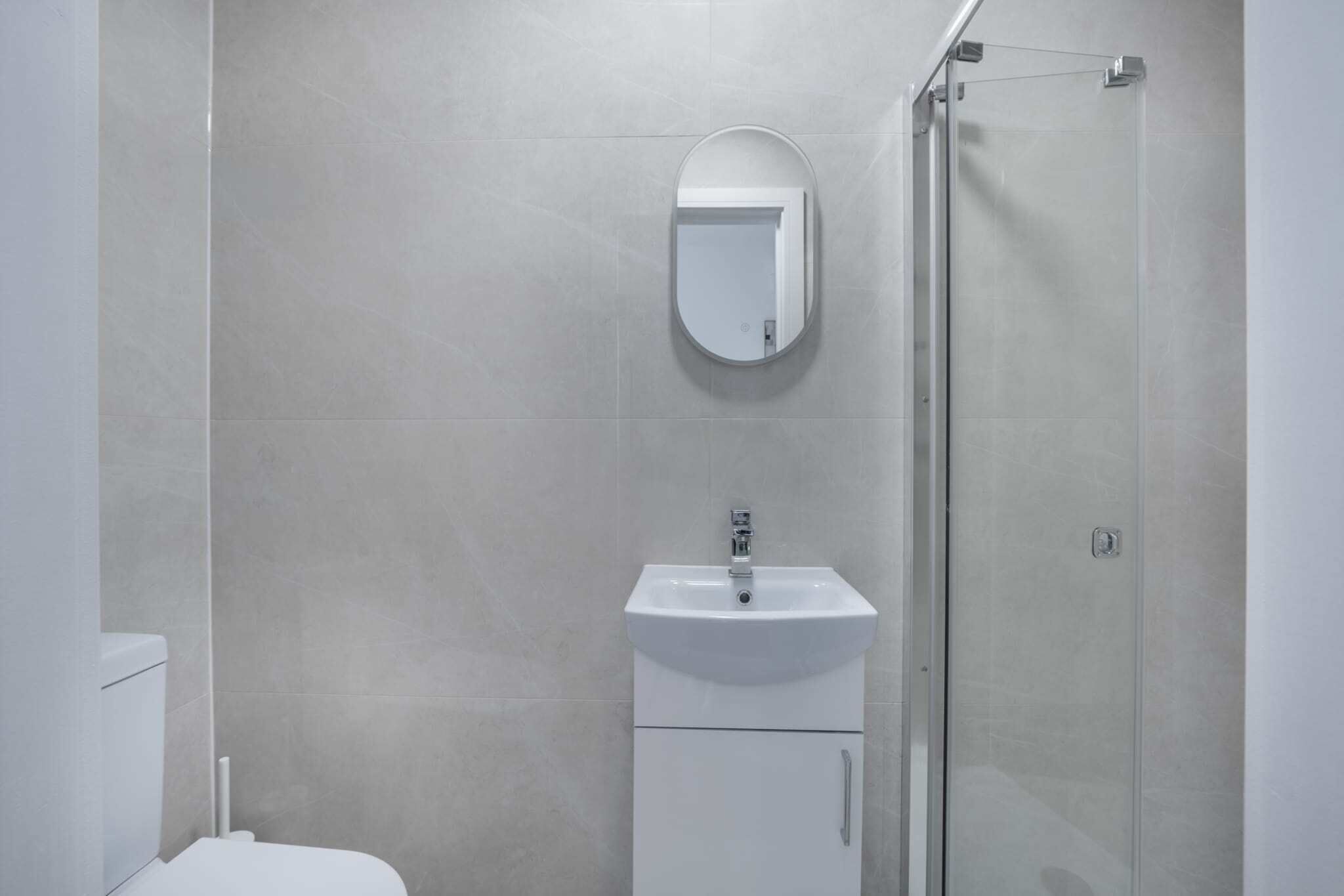 A bathroom with a toilet, a sink, a mirror, and a glass shower enclosure.