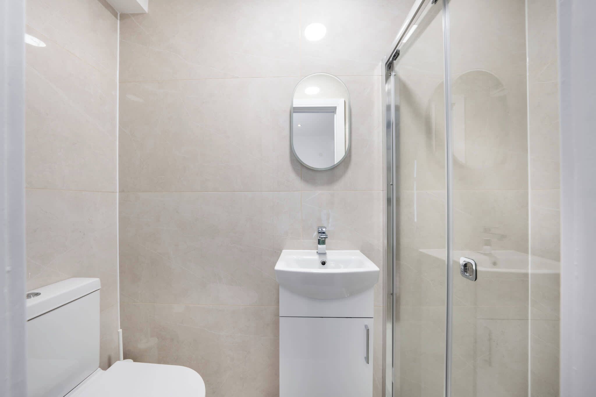 Ein modernes Badezimmer mit Toilette, Waschbecken mit Spiegel und einer Duschkabine aus Glas.