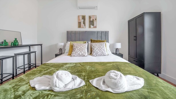 Een hotelkamer met een bed, twee nachtkastjes, een bureau met stoelen, een kledingkast en een airconditioning.