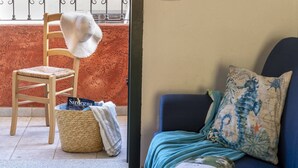 Ein Zimmer mit einem Holzstuhl, einem gewebten Korb, einer Couch mit einem gemusterten Kissen und Blick auf eine rote Wand und einen Balkon.