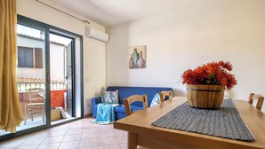 Ein Zimmer mit Esstisch, Stühlen, einer Couch, einer Schiebetür aus Glas und einem Blumentopf.