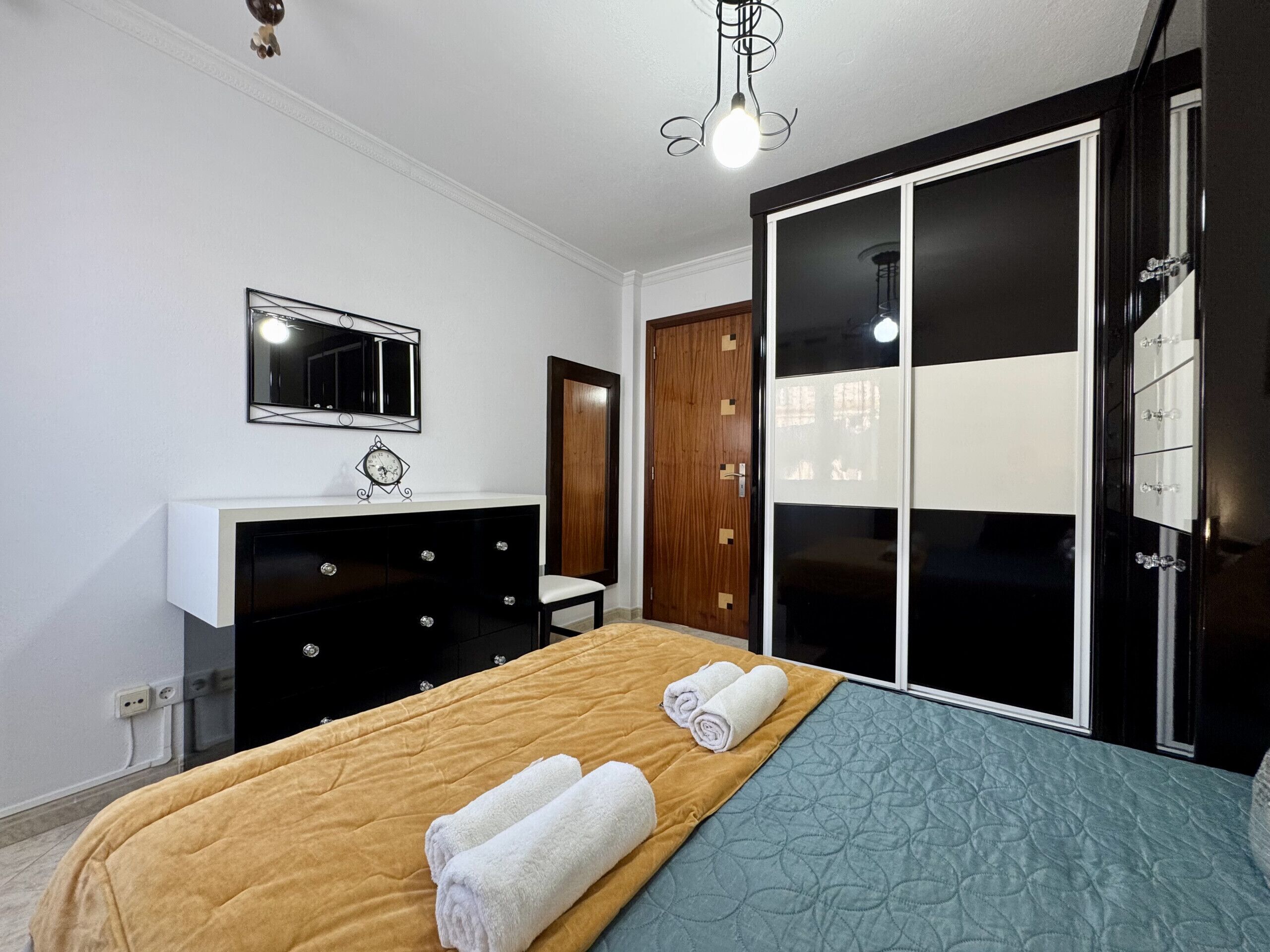 A bedroom with a bed, a dresser, a mirror, a wardrobe, and a light fixture.