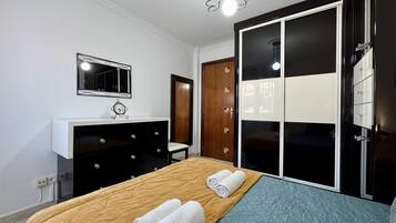A bedroom with a bed, a dresser, a mirror, a wardrobe, and a light fixture.