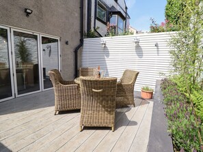 Eine Terrasse mit Korbmöbeln, einem Blumentopf und einer weißen Wand.