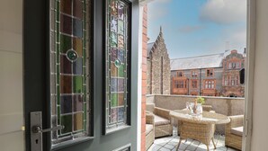 Una puerta con vidrieras, un balcón con mobiliario de mimbre y vistas a edificios tradicionales.