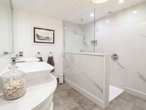 Ein modernes Badezimmer mit Duschkabine aus Glas, einem großen weißen Waschbecken und einem gerahmten Bild an der Wand.
