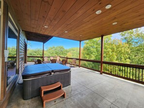 A covered outdoor deck with a hot tub, seating, and a view of trees. - Luxury 15BR Cabin w/ Indoor Pool, Theater, Hot Tubs, Sleeps 64 Guests (Sevierville)