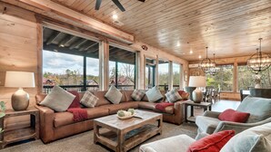 Ein geräumiges Wohnzimmer mit Holzboden, großen Fenstern und einer gemütlichen Sitzecke mit Sofa und Sesseln.