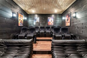 A cinema with wooden walls, black leather seats, and movie posters on the walls. - Luxury 15BR Cabin w/ Indoor Pool, Theater, Hot Tubs, Sleeps 64 Guests (Sevierville)