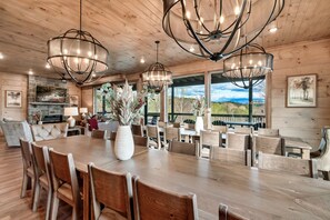 A spacious dining area with a large wooden table, multiple chairs, and modern chandeliers. - Luxury 15BR Cabin w/ Indoor Pool, Theater, Hot Tubs, Sleeps 64 Guests (Sevierville)