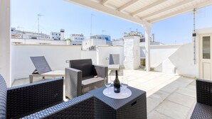 An outdoor patio with wicker furniture, a bottle of wine, and glasses on a table.