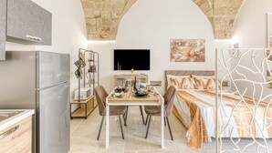 A compact room with a kitchenette, a dining area, a bed, and a TV.