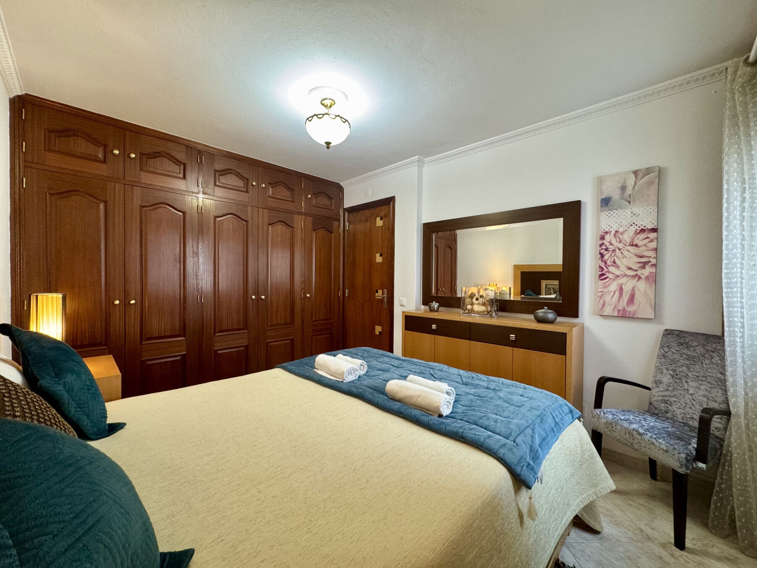 Une chambre d’hôtel avec un lit, une commode, une chaise et un grand miroir.