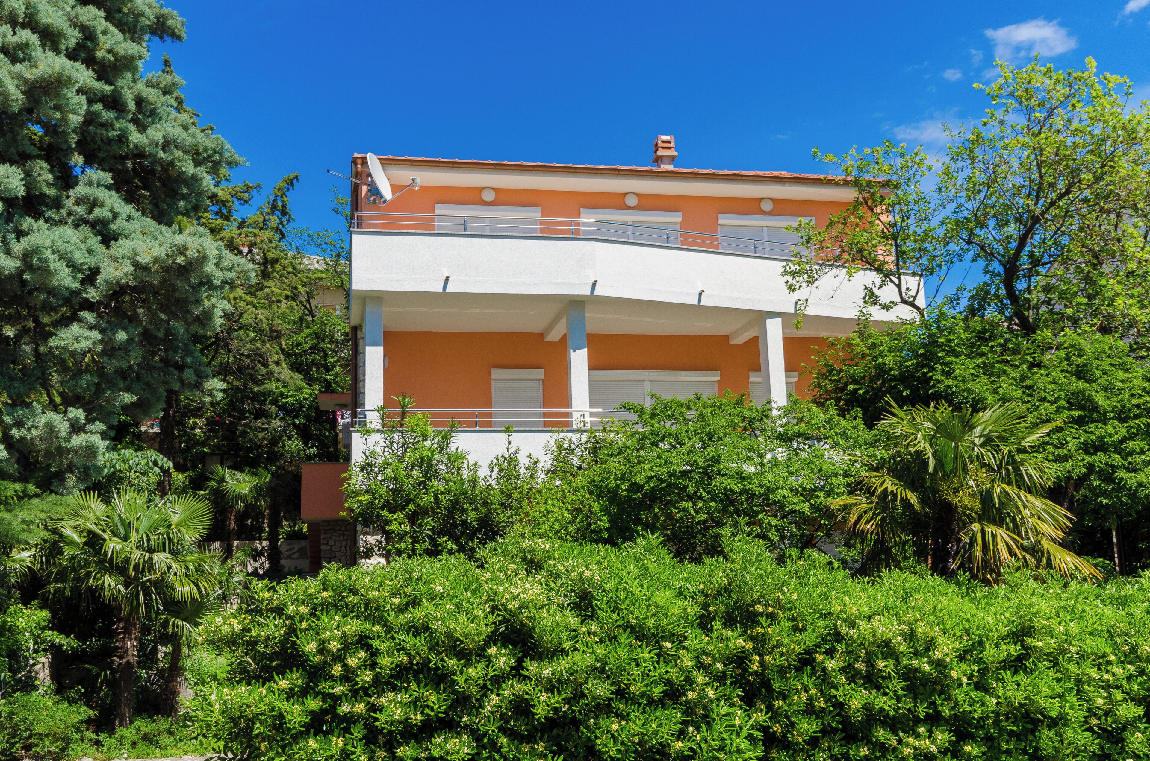 A two-story building with a balcony, surrounded by dense greenery.