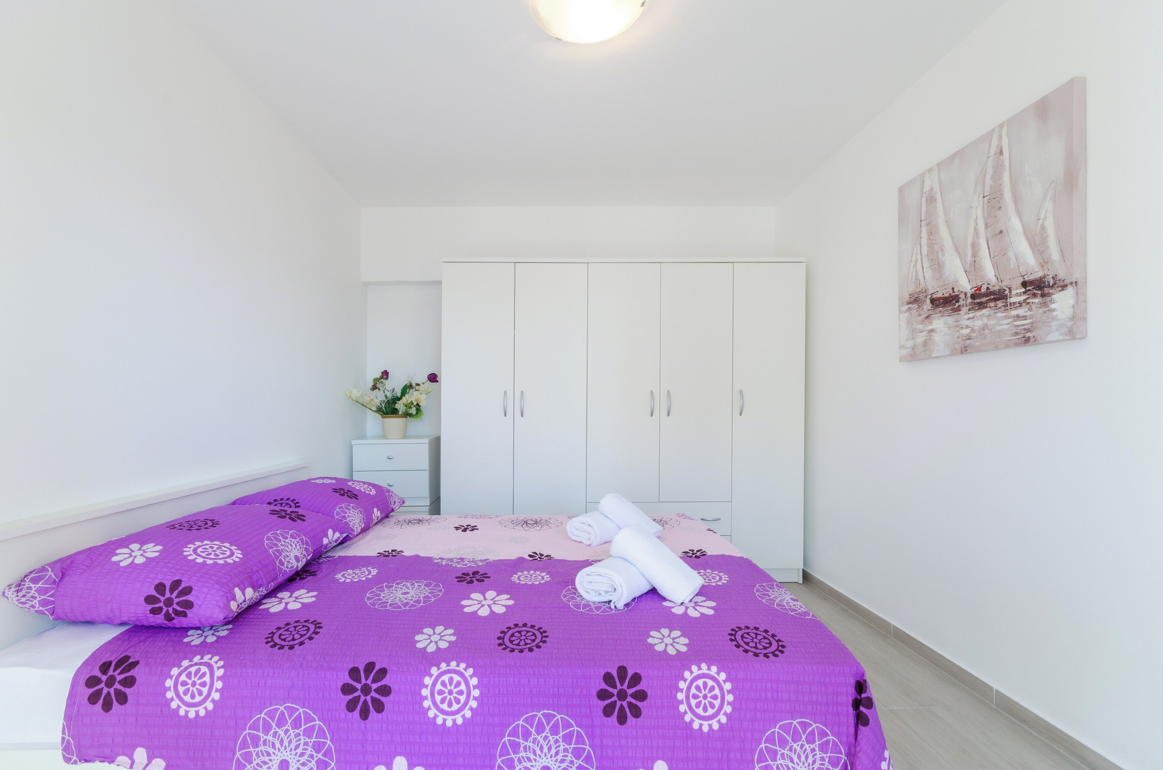 A bedroom with a bed, pillows, a nightstand, a mirror, and a wardrobe.
