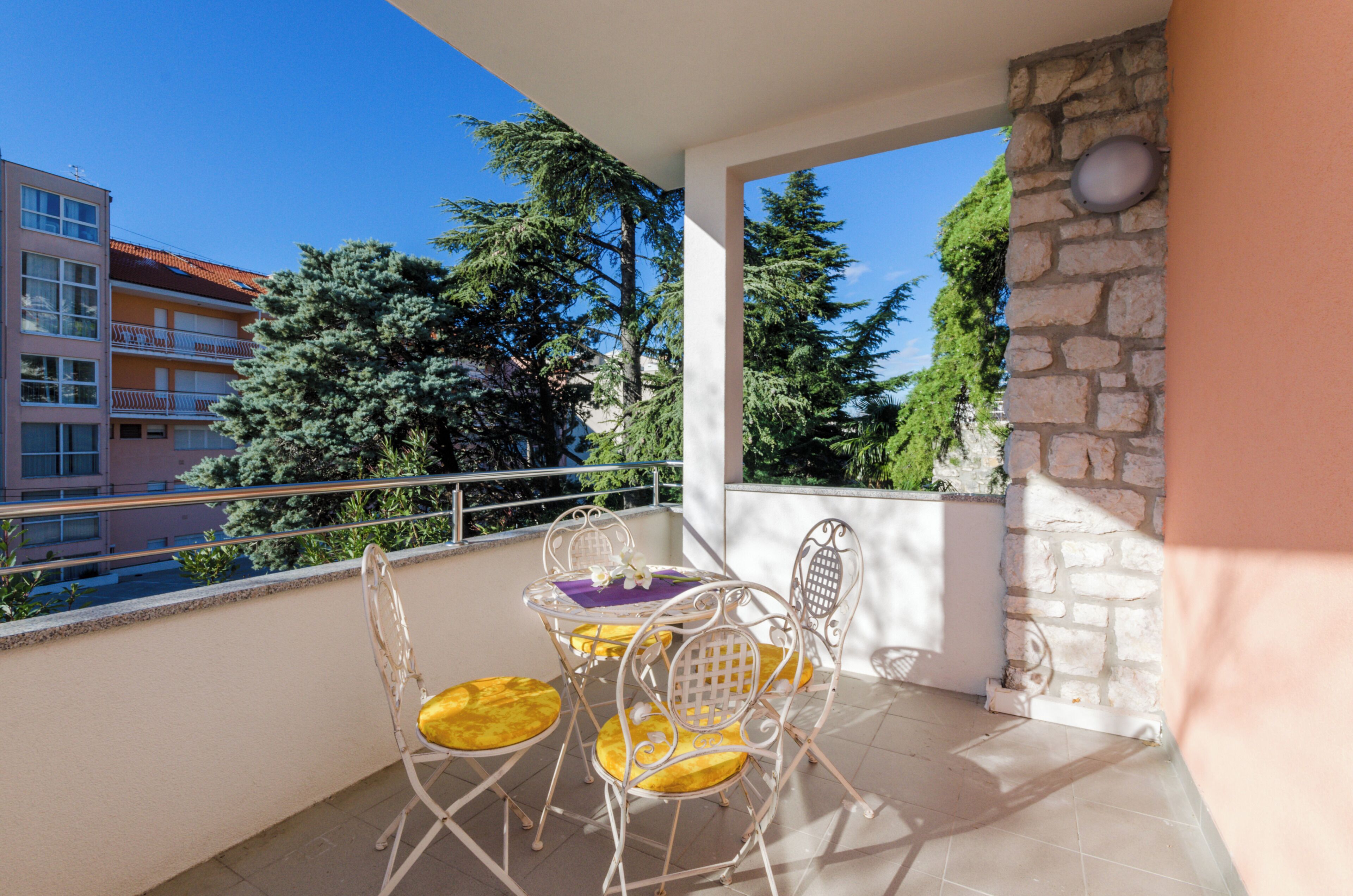 Un balcon avec une table et des chaises, un mur en pierre et une vue sur des immeubles et des arbres.