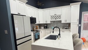 A modern kitchen with white cabinetry, a central island, a built-in oven, and a stainless steel refrigerator.