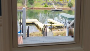 A view through a window of a dock extending into a body of water, with a house and greenery in the background.