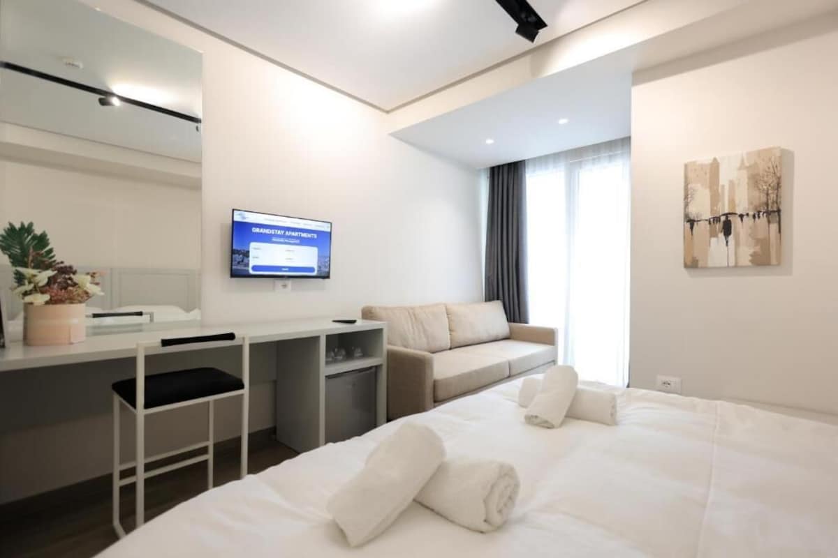 Una habitación de hotel moderna con una cama, un escritorio, una silla, un televisor y una ventana con cortinas.