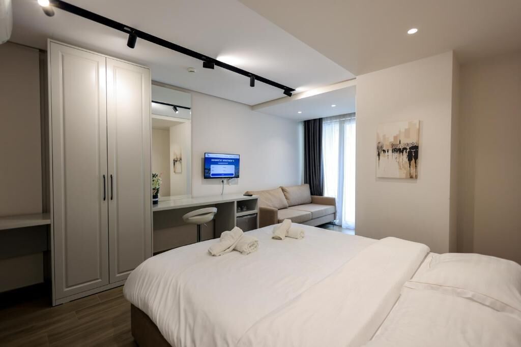 A modern hotel room with a large bed, a desk, a wardrobe, a television, and a painting on the wall.