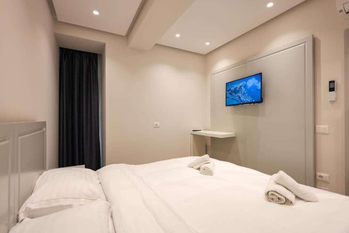 Una habitación de hotel con una cama, un televisor montado en la pared y una mesita de noche.