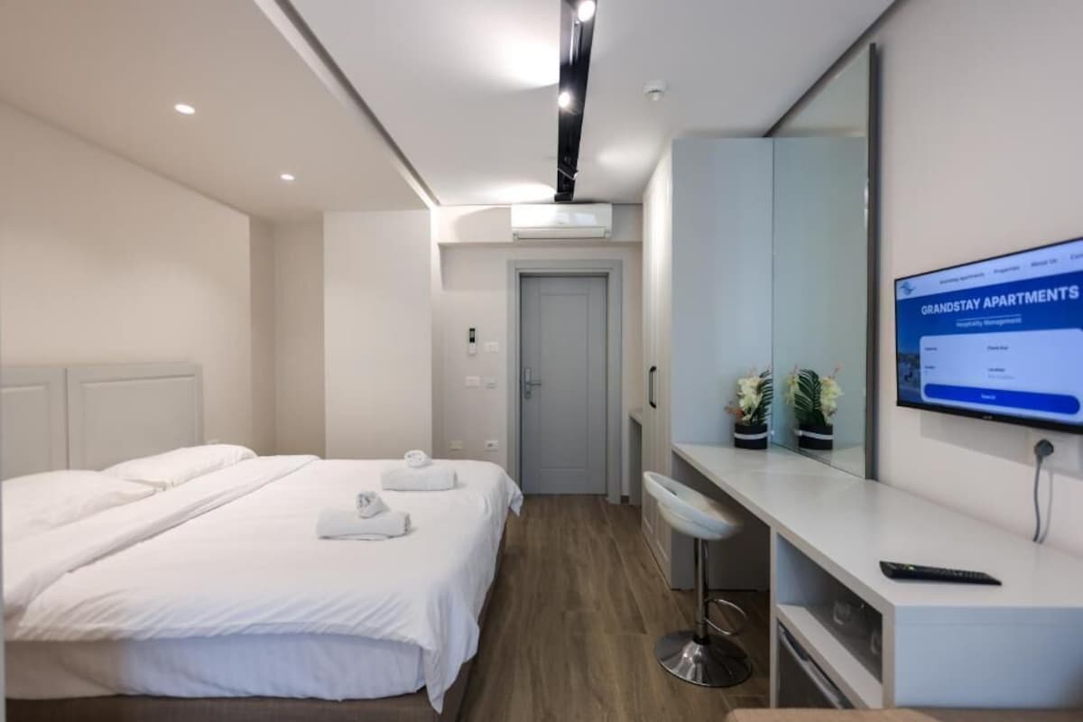 Una habitación de hotel moderna con una cama, un escritorio, una silla, un televisor y un equipo de aire acondicionado.