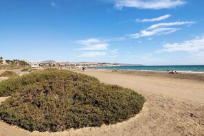 Une plage avec une zone de sable, quelques espaces verts et des bâtiments situés au loin.