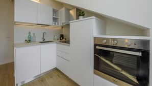 Une cuisine compacte avec des meubles blancs, un four encastré et un petit plan de travail sur lequel sont disposés divers objets.
