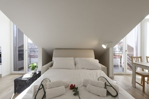 A bedroom with a large bed, a dining table, and a view through a sliding door. - NOVARA, 6 - In the attic with style (Milan)