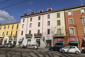 A row of multi-story buildings with various shops and businesses on the ground floor. - NOVARA, 6 - In the attic with style (Milan)