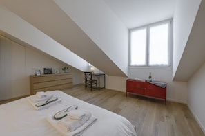 A bedroom with a sloped ceiling, a bed with neatly folded towels, a wooden dresser, a red cabinet, and a small table with a lamp. - NOVARA, 6 - In the attic with style (Milan)