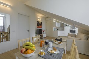 A modern kitchen with white cabinets, a dining table set with fruits, a coffee maker, and a TV. - NOVARA, 6 - In the attic with style (Milan)