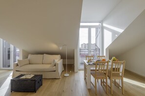 En moderne loftlejlighed med højt til loftet, en sofa, et spisebord med stole og et stort vindue med udsigt over byen.