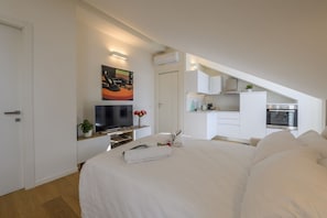 A modern bedroom with a large bed, a TV, and a kitchenette in the background. - NOVARA, 6 - In the attic with style (Milan)